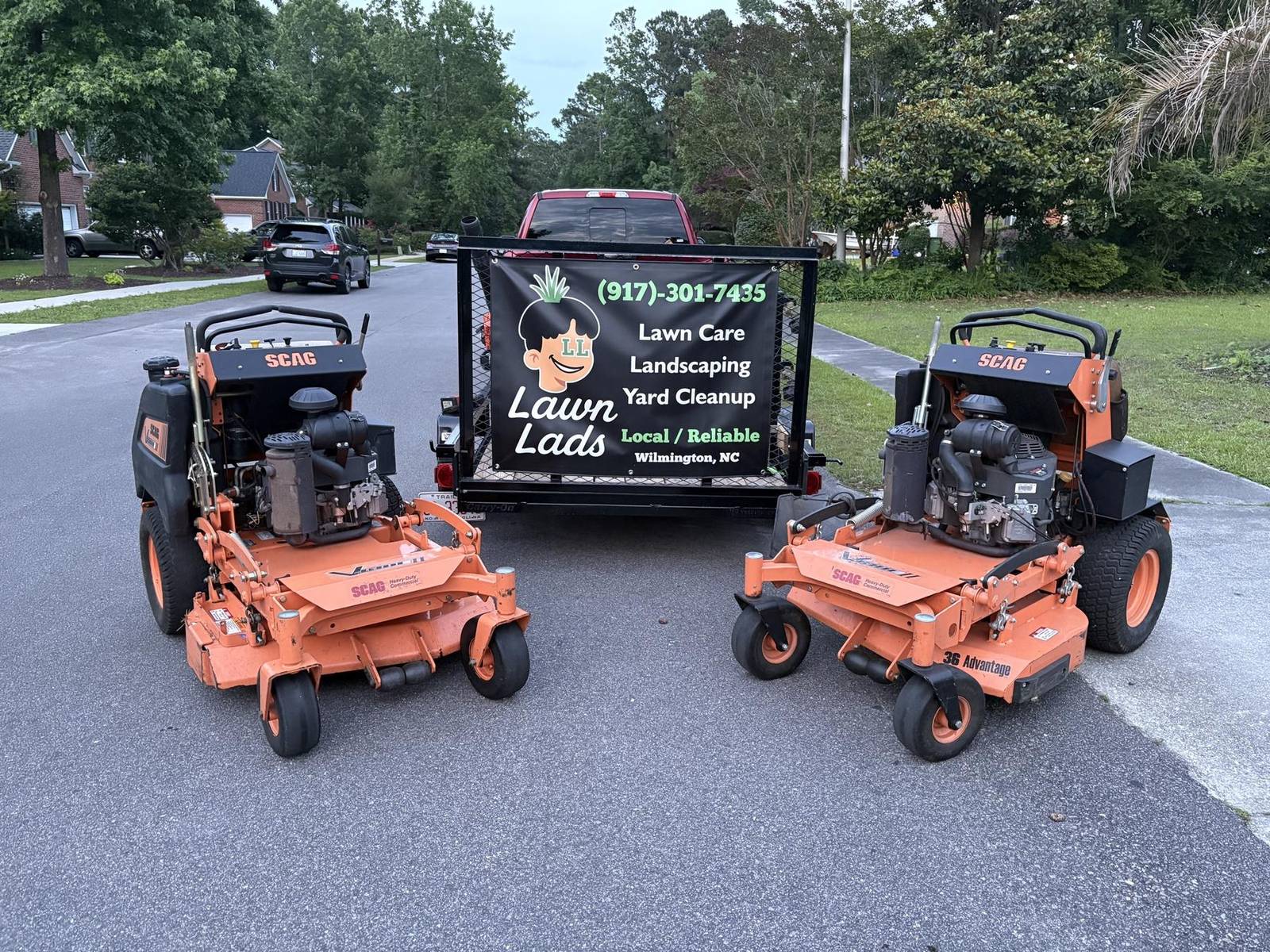Two Scag stand-on mowers beside the Lawn Lads trailer sign