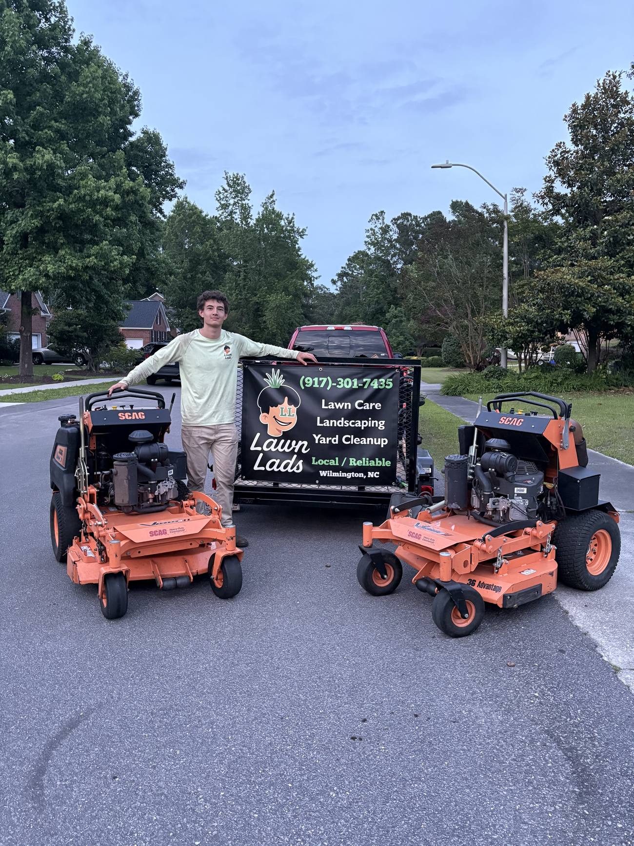 A Lawn Lads owner standing between the two Scag mowers in front of the branded trailer